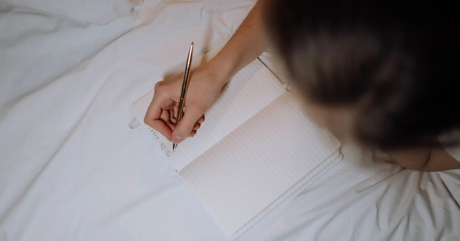 Mano escribiendo en un cuaderno sobre ropa de cama blanca